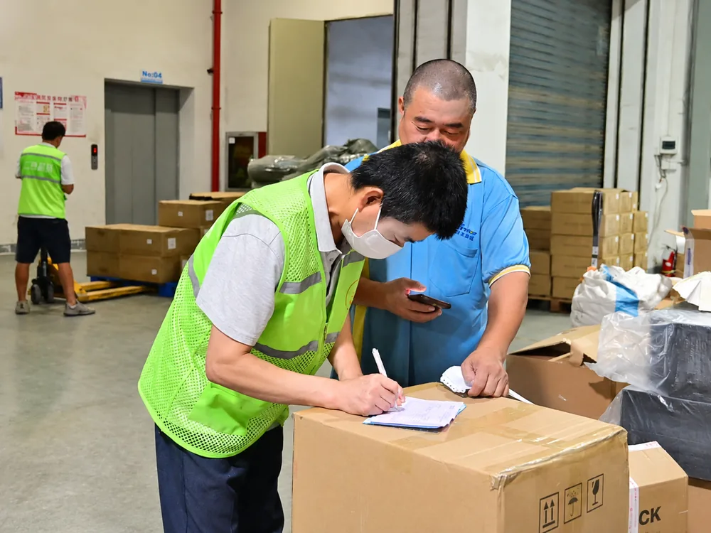 Warehouse staff checking shipment paperwork beside packed cartons at a HUIXIN 3PL China warehouse